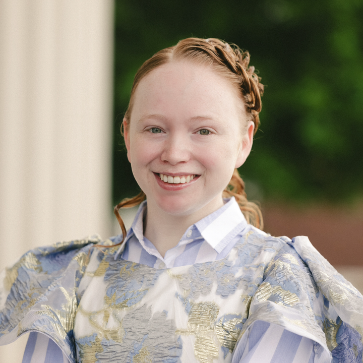 Smiling person in a blue-and-gold patterned outfit outdoors with a blurred green background