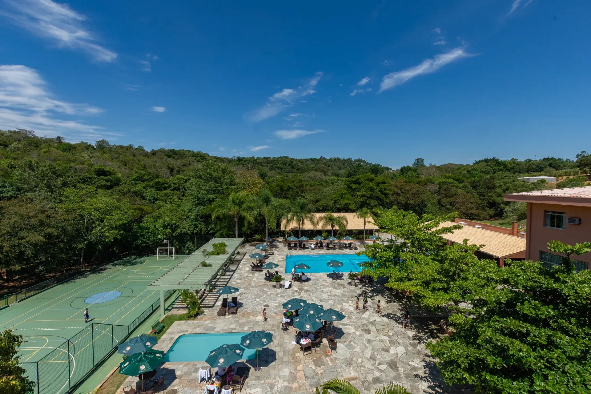 uma vista aérea de uma quadra de tênis e uma piscina cercada por árvores.