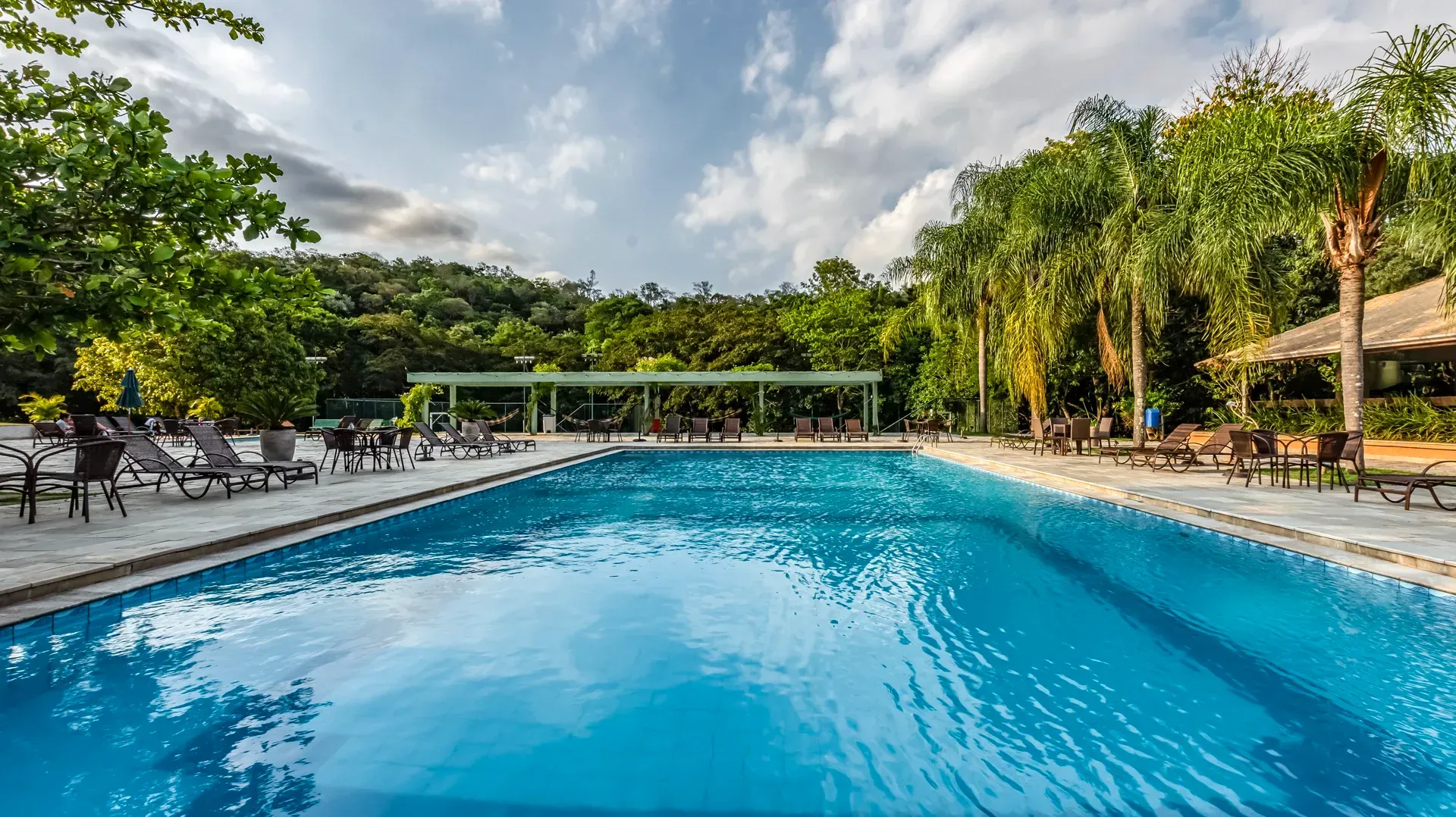 uma grande piscina cercada por árvores e cadeiras em um dia ensolarado.