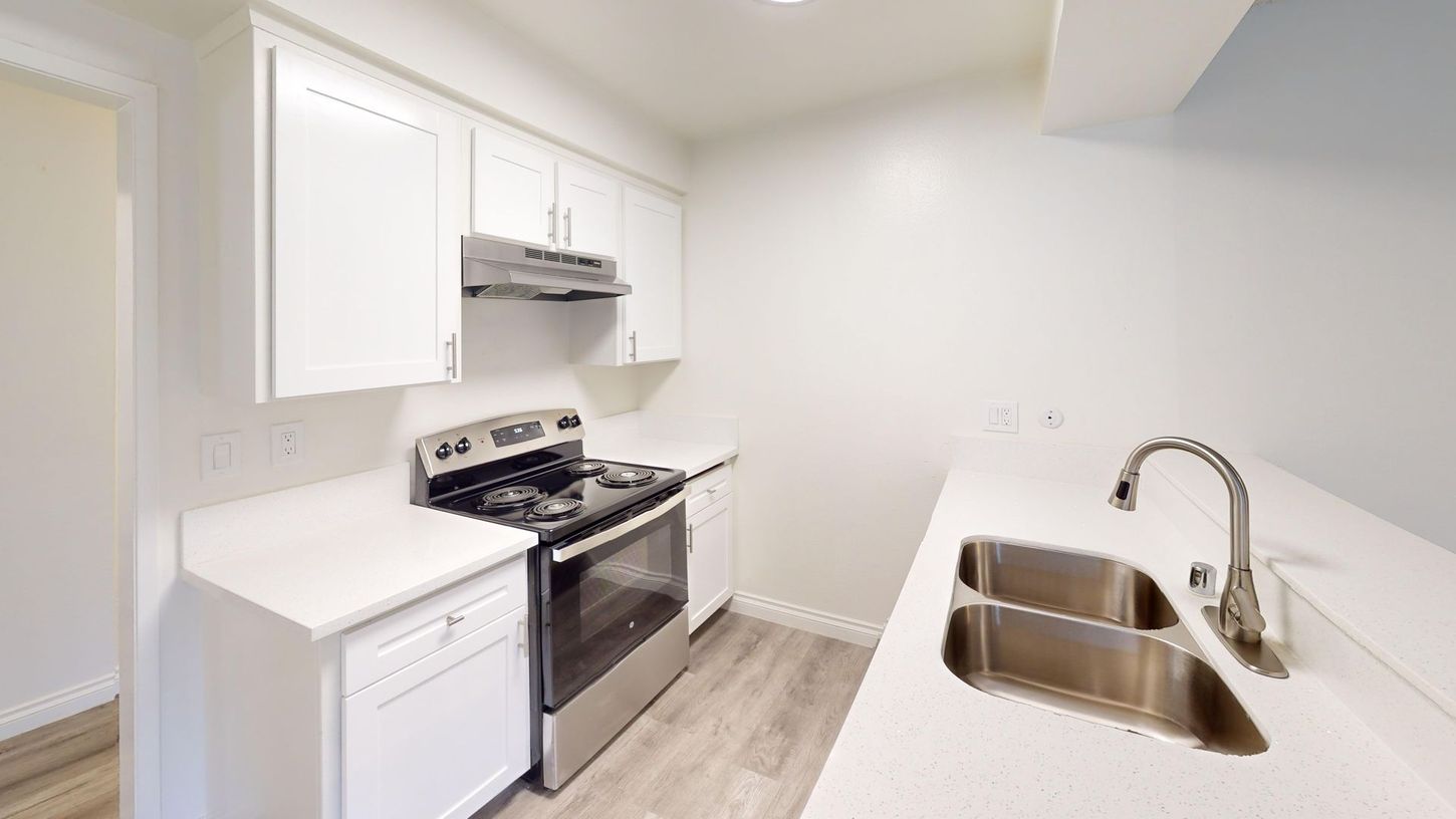 White kitchen with stainless steel appliances, countertops, and a sink.