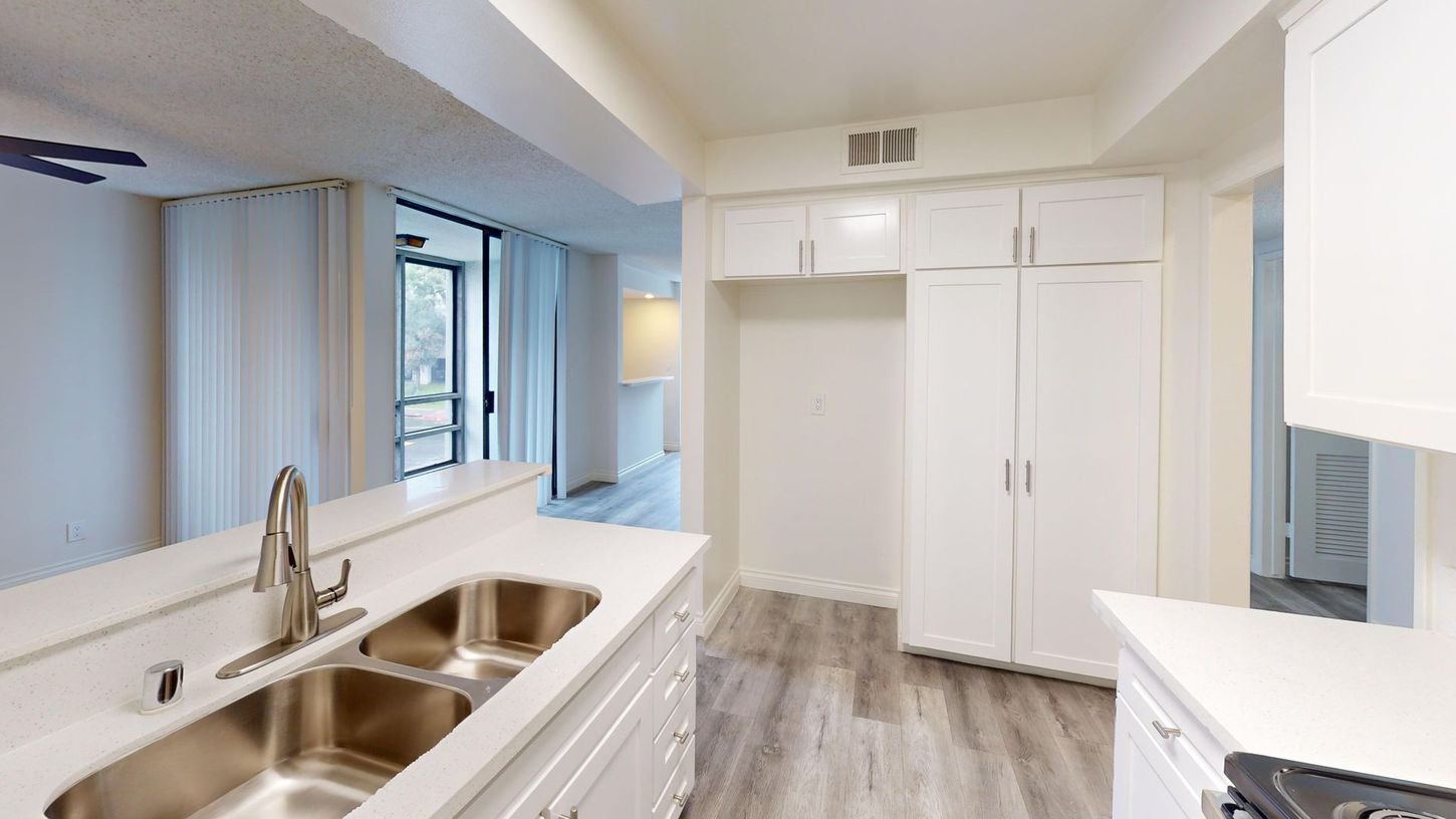 Kitchen with white cabinets, silver sink, and grey wood-look flooring.