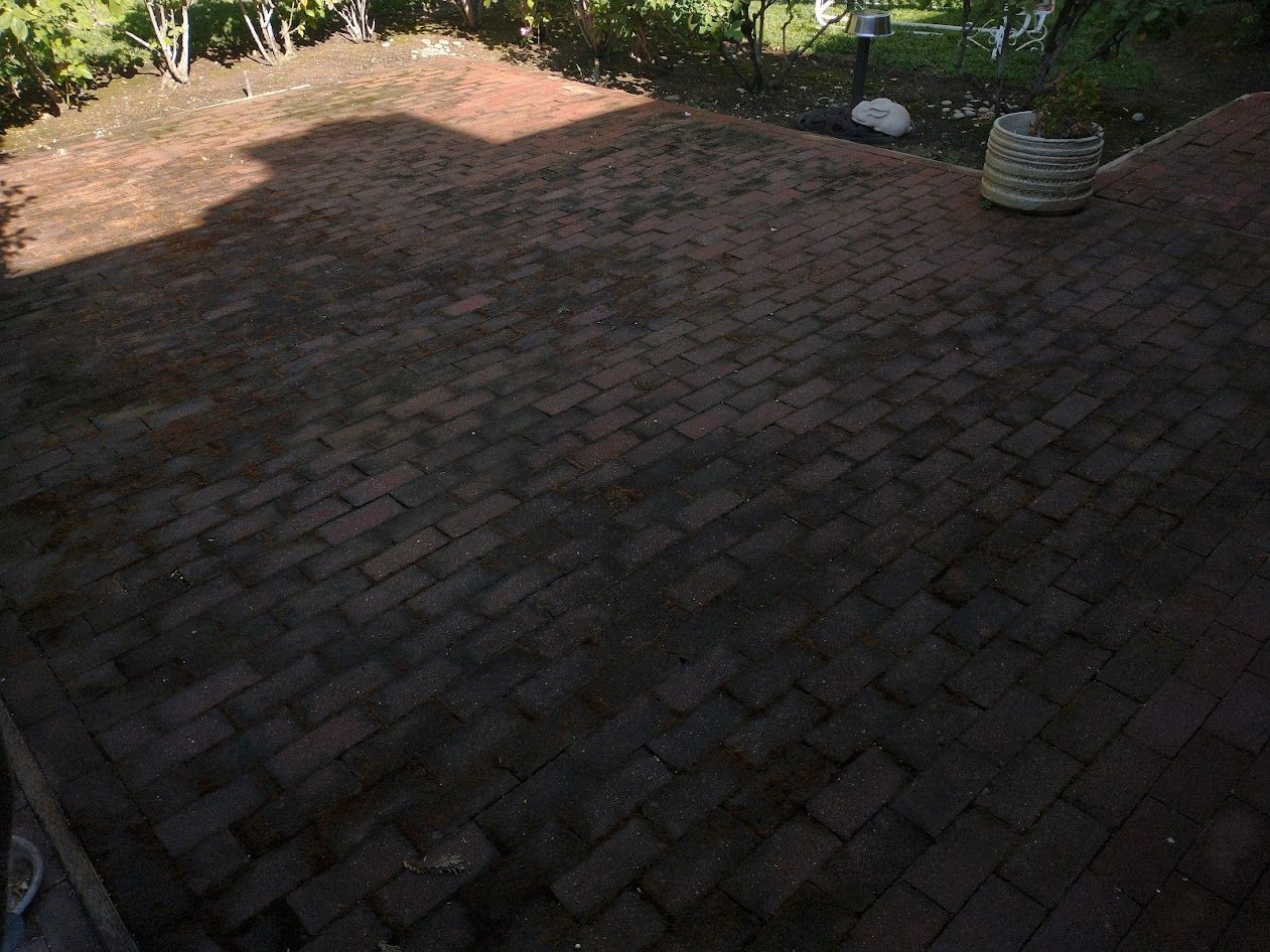 A brick patio in a backyard with patchy grass and a small decorative planter.