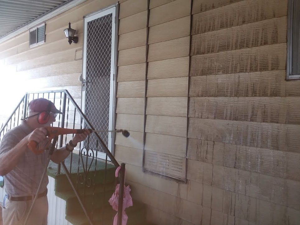 A person using a pressure washer to clean the exterior siding of a house.