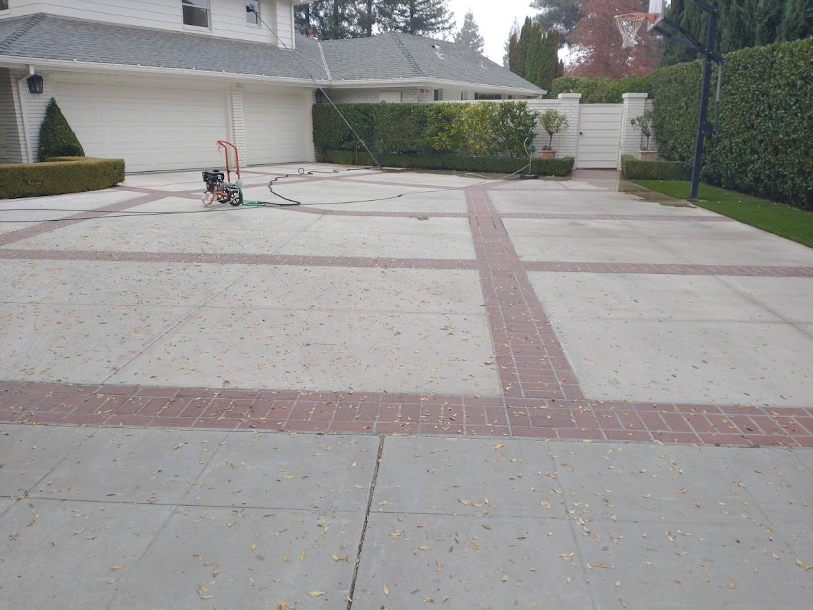 A concrete driveway with red brick inlay patterns leads toward a two-car garage and a gated entryway.