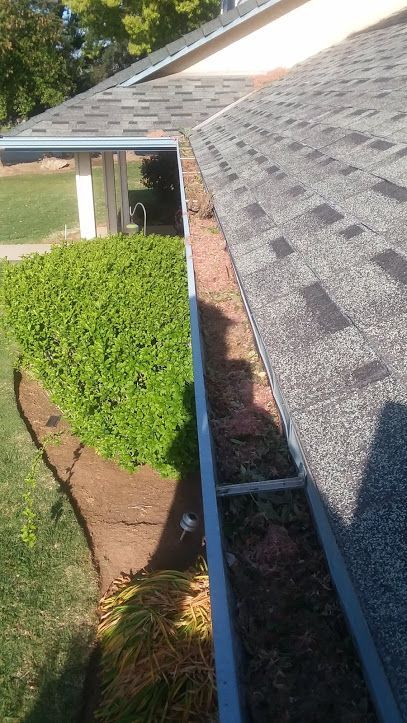 A high-angle view showing a residential roof gutter filled with dead leaves and debris along the roof's edge.