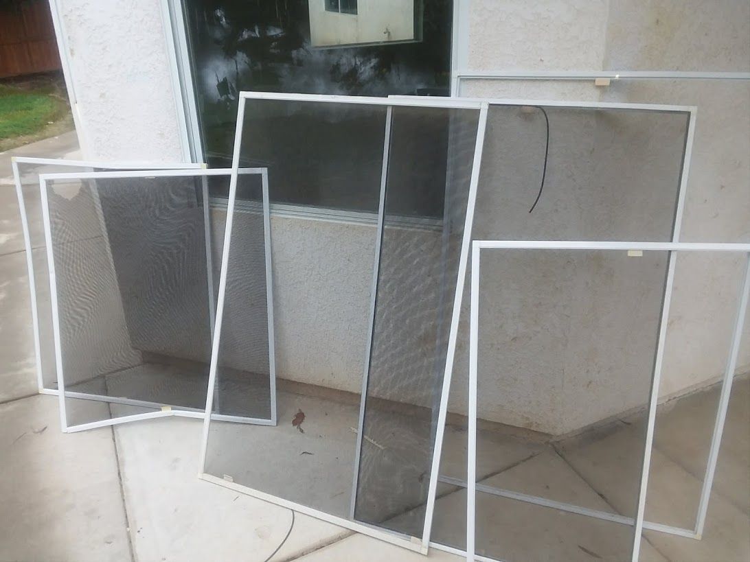 Several white-framed window screens lean against a textured wall outside near a glass window.