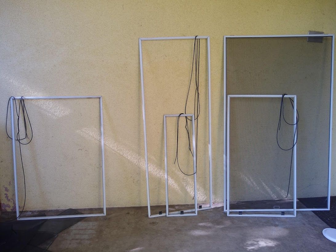 Five white empty or mesh window screen frames leaning against a light-colored wall.