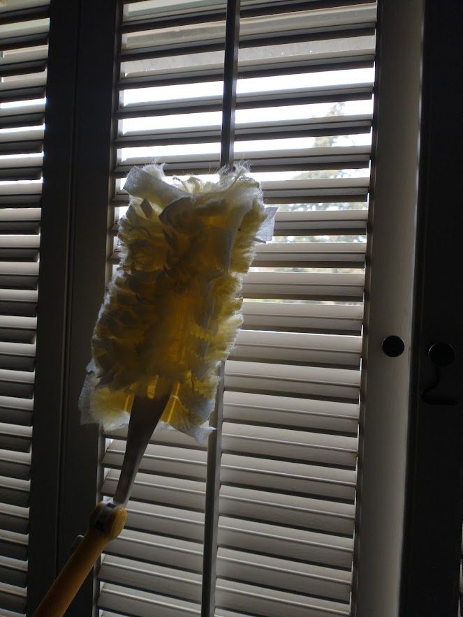 A yellow duster cleaning between the slats of white window shutters.