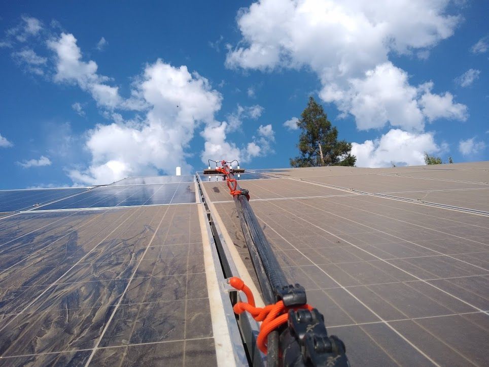 A bright orange rope is threaded through a black metal track running between solar panels under a bright, cloudy sky.