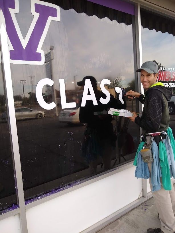 A window washer smiles while cleaning a glass storefront that features a large purple 