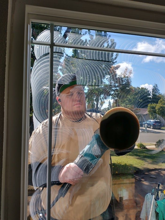 A person cleaning a window with a circular buffing tool, creating swirling patterns in the cleaning solution.