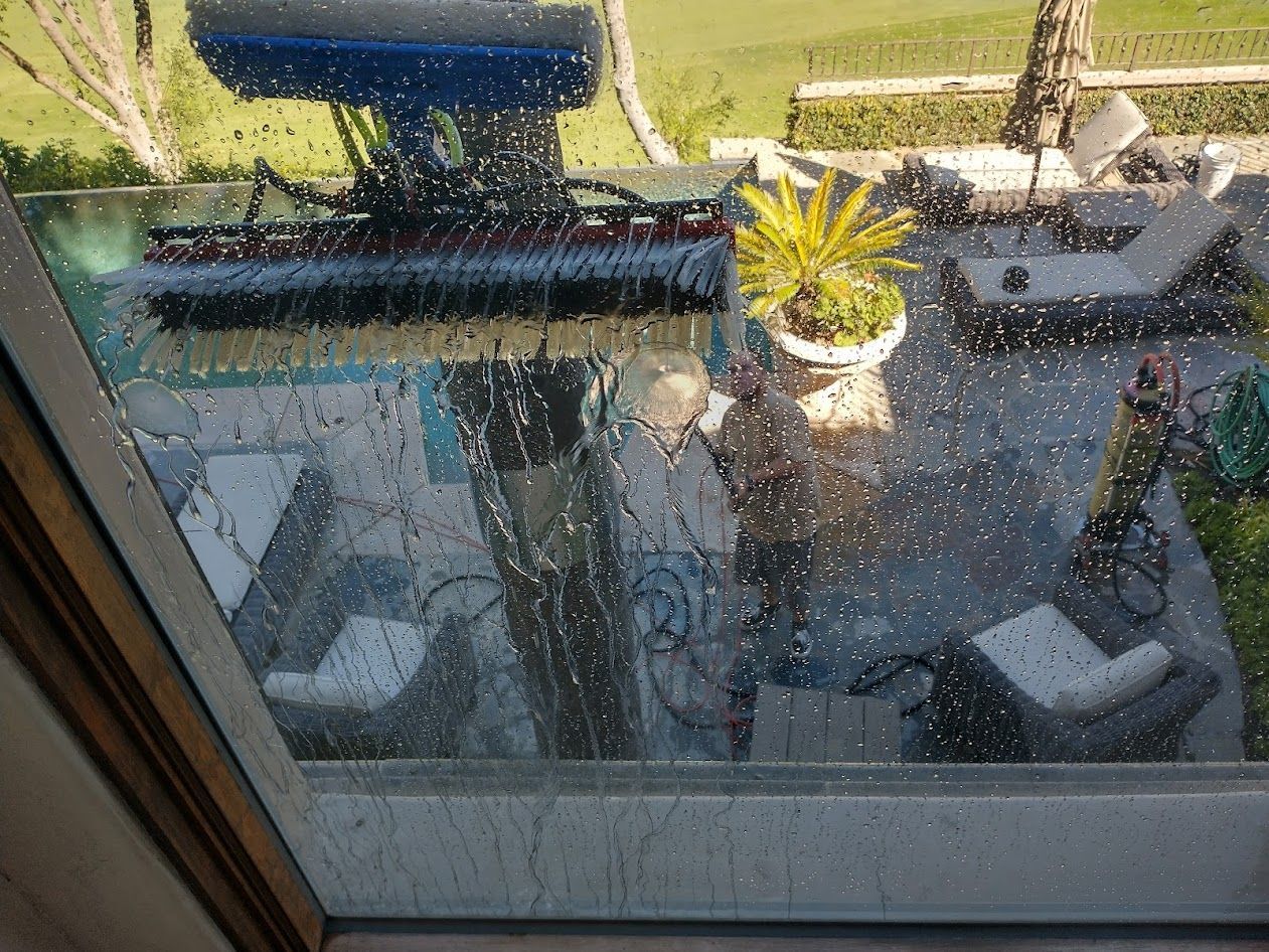 A window cleaning brush tool being used to clean a glass door from the outside, with a patio visible in the background.