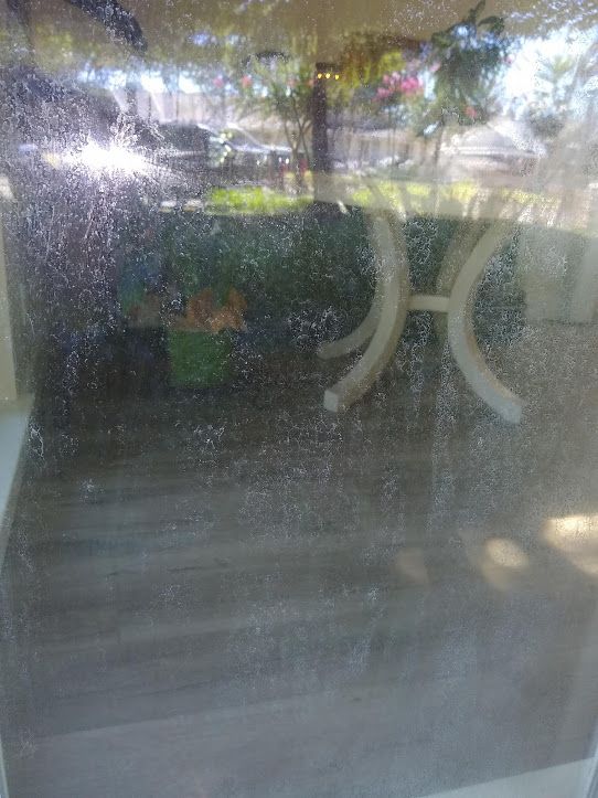 A large glass pane with a widespread pattern of white, misty water spots or mineral buildup, obscuring the view outside.