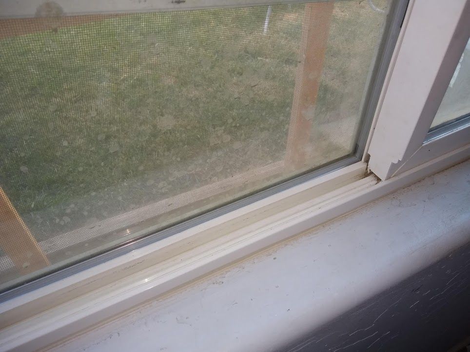 A close-up view of a white vinyl window frame and sill, showing the sliding track and a screen with a grassy lawn outside.