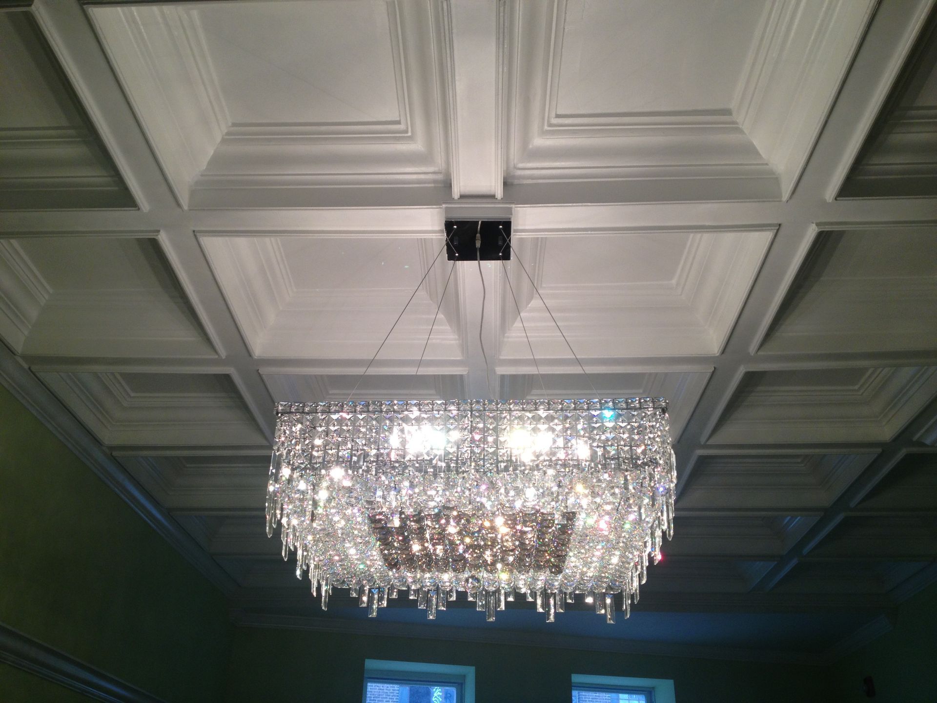 White coffered ceiling with layered mouldings and a rectangular crystal chandelier