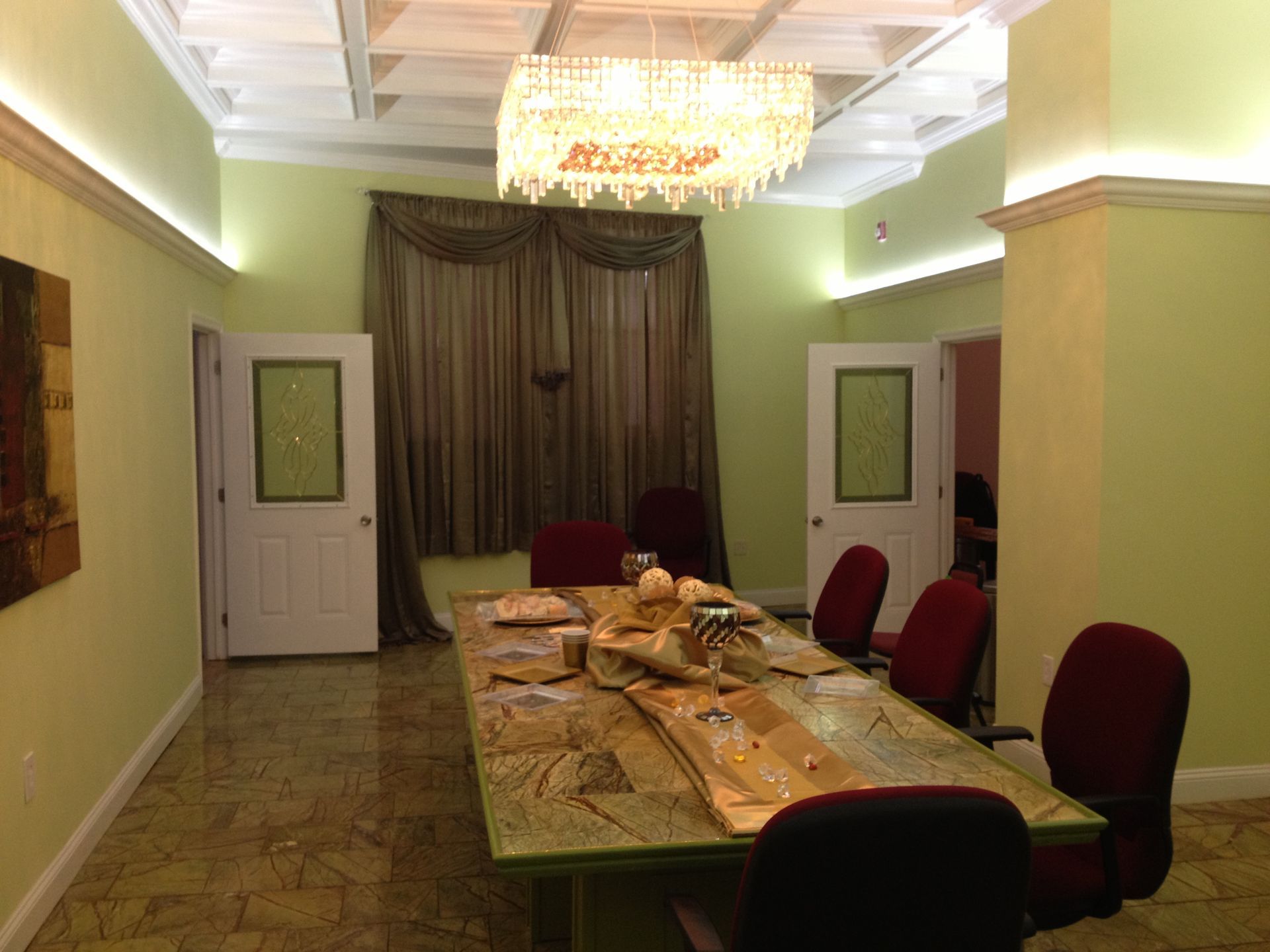 Dining room with a coffered ceiling, crystal chandelier, green walls and full-length curtains