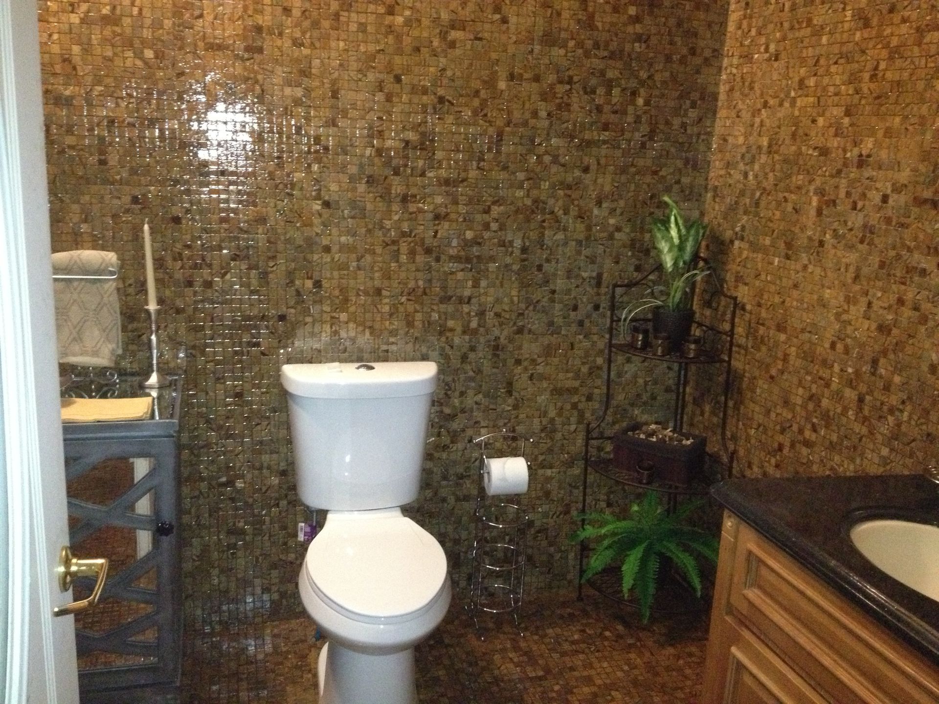 Bathroom with gold-toned mosaic tile walls, a white toilet and a wood vanity with a dark countertop