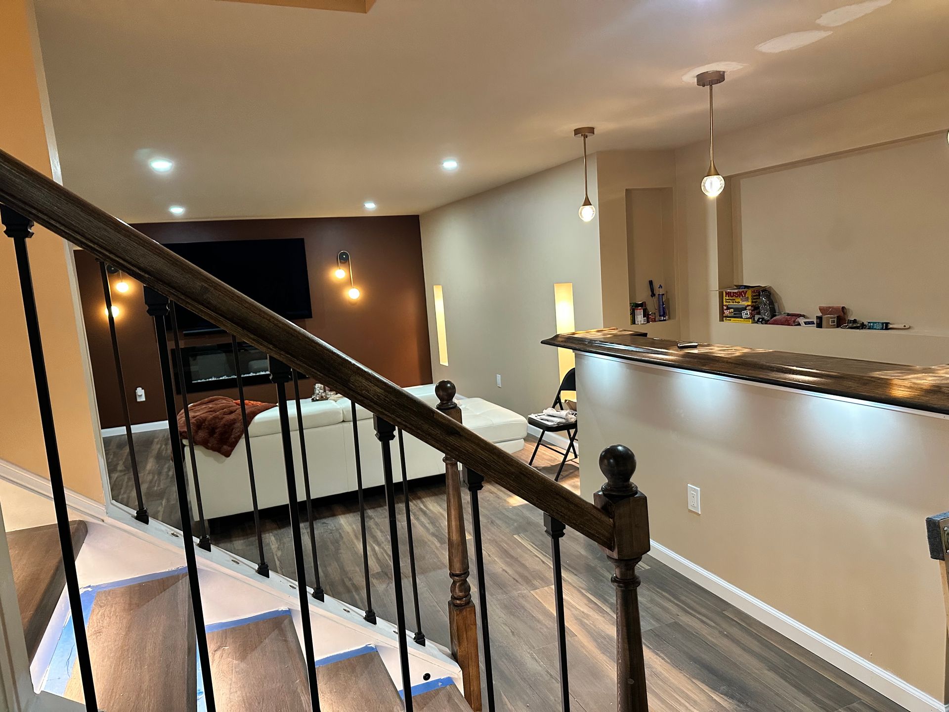 View across a finished living area from the staircase, with a long counter and recessed lighting