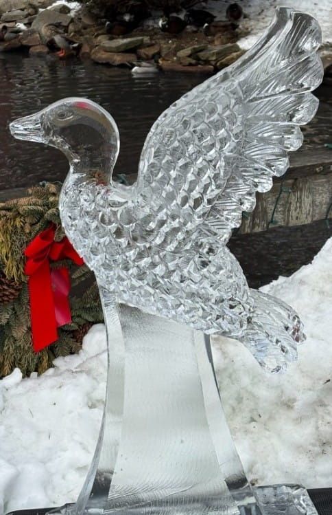 Clear ice swan sculpture with red ribbon, displayed outdoors in snow