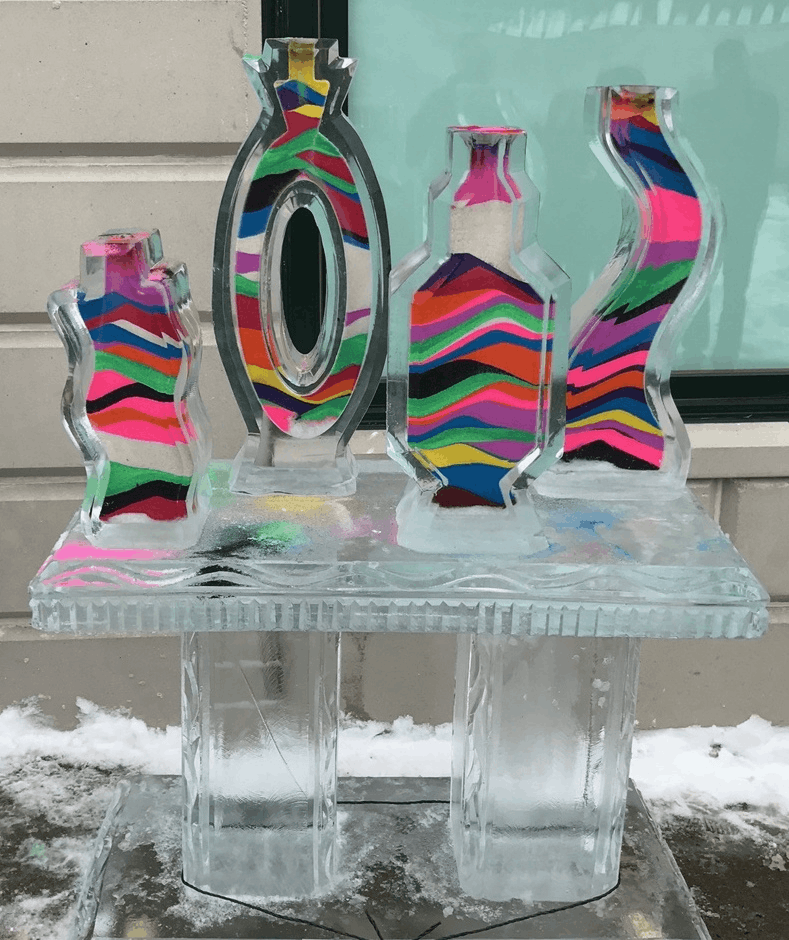 Colorful striped ice sculptures on clear blocks outdoors with snow in the background