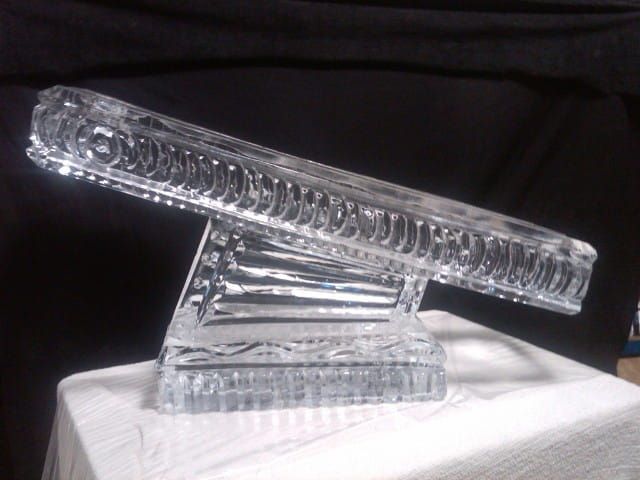 Clear glass slanted sculpture on a white base against a black background