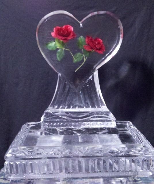 Clear glass heart sculpture with two red roses inside on a base