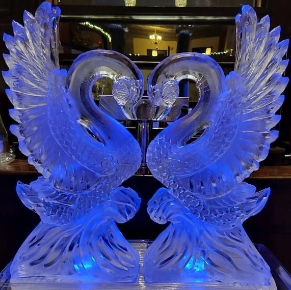 Blue swan-shaped ice sculpture with wings spread, facing each other in a lit indoor display