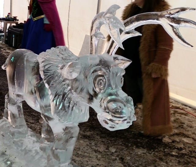 Clear ice sculpture of a wolf or deer on a counter, with a blurred person in the background