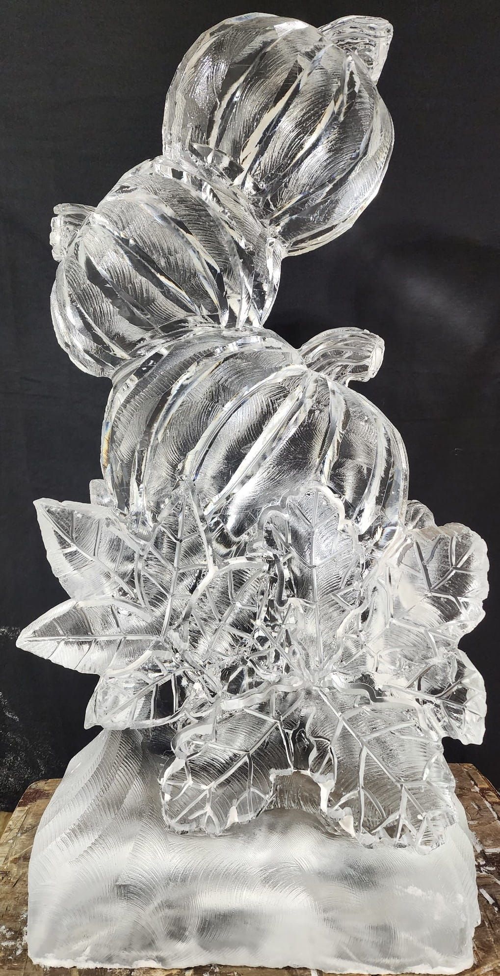 Clear crystal sculpture of stacked glass-like forms on a small base against a dark background