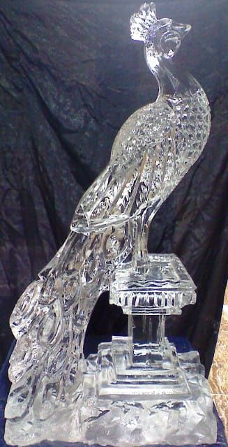 Clear glass crystal bird sculpture on a small pedestal, with textured feathers and a raised crest.