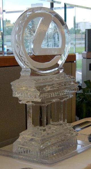 Clear glass award trophy with a circular top on a faceted pedestal, displayed indoors.