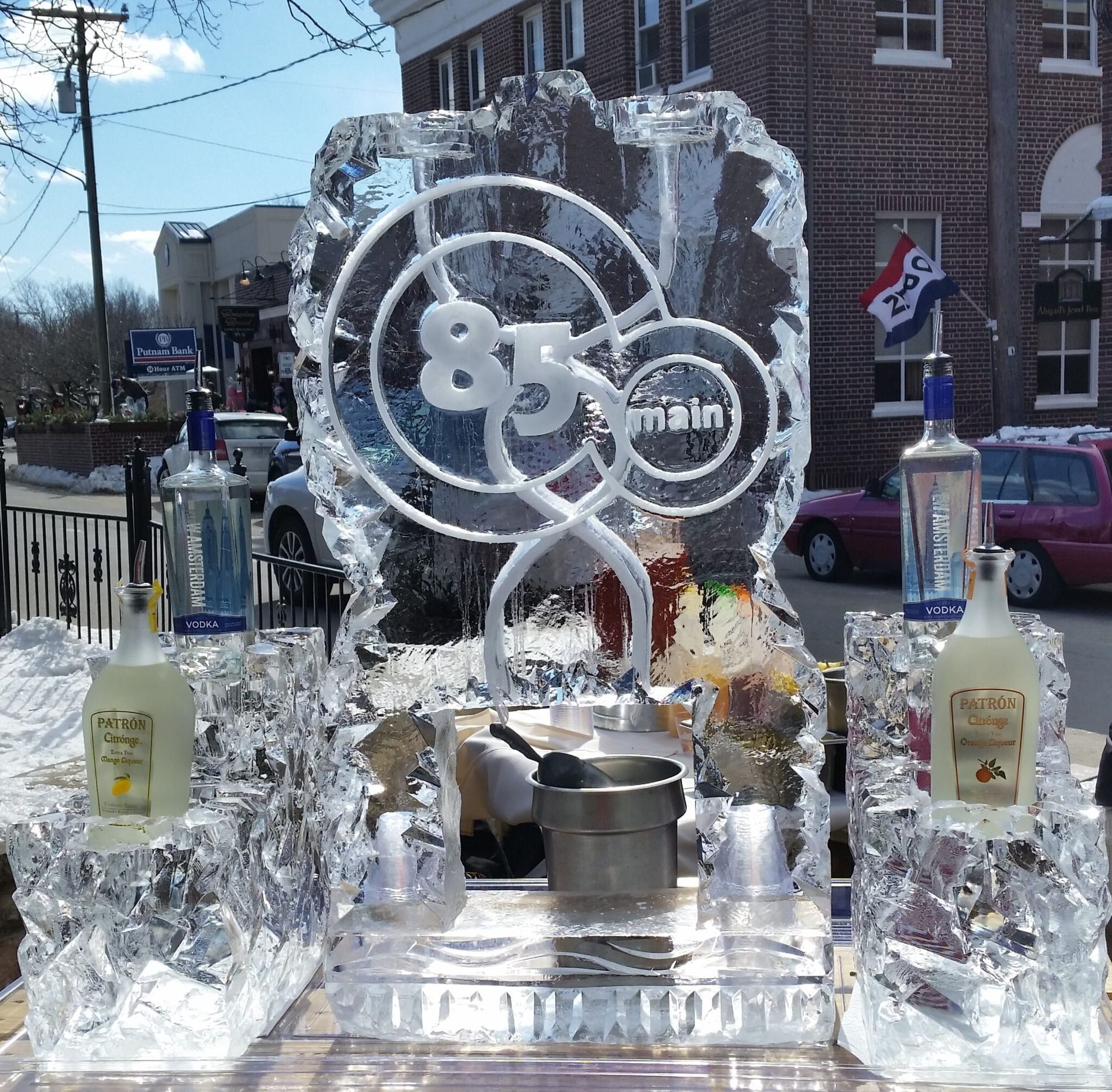Ice sculpture with Olympic rings and liquor bottles displayed outdoors in front of a brick building.