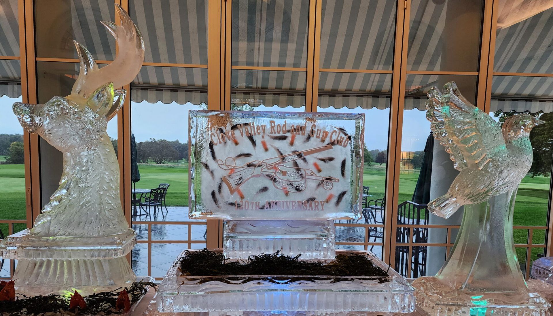 Ice sculptures of deer flank a fish display on a table in front of a windowed dining hall.