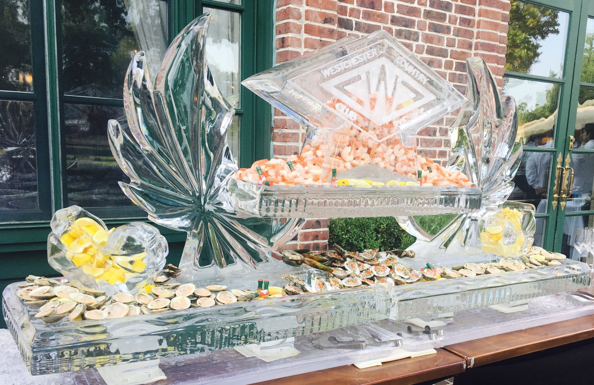 Clear ice sculpture centerpiece with fruit on a table outside a brick building