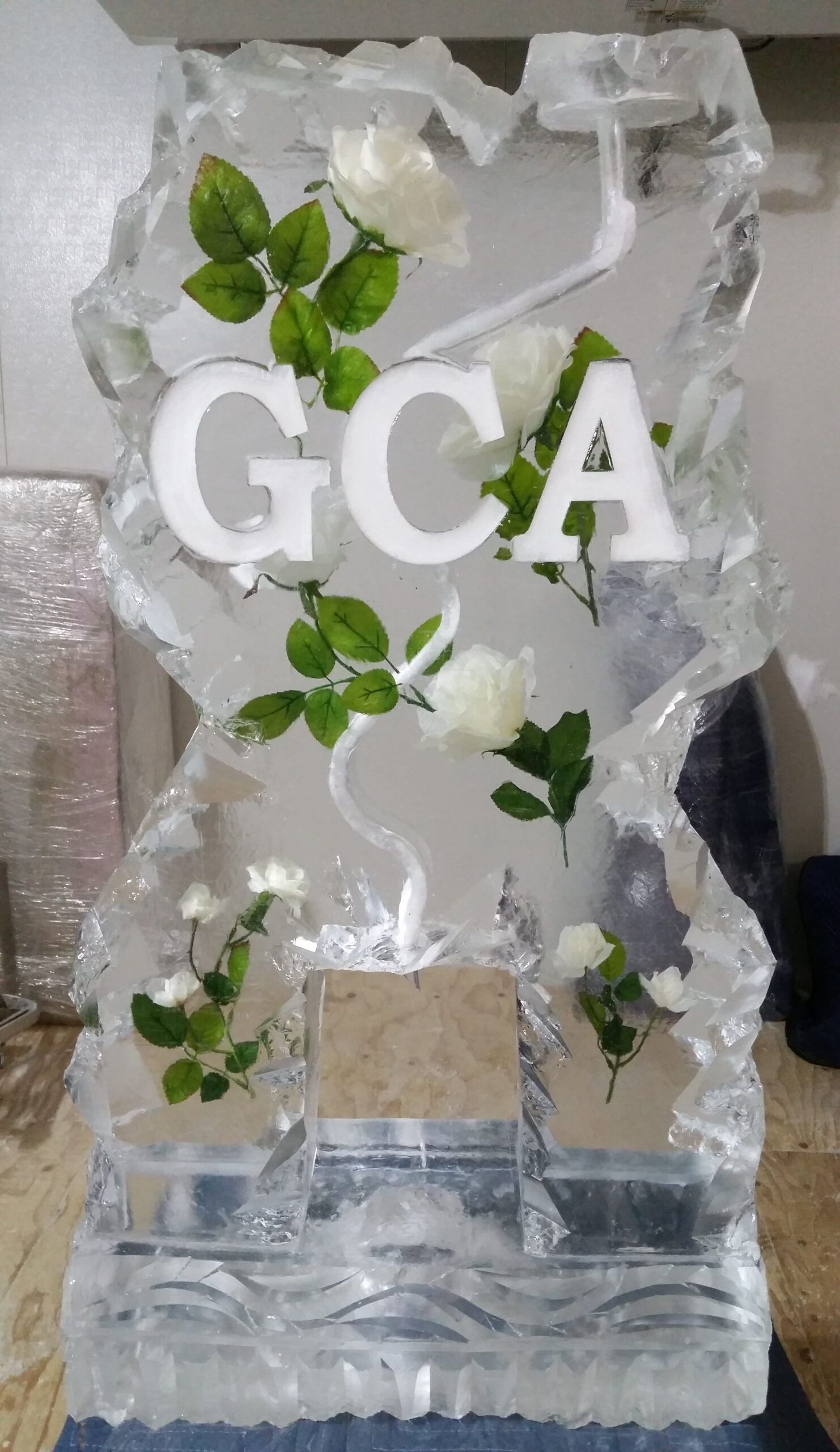 Clear decorative award plaque with white “GCA” letters and green leaves on a textured base.