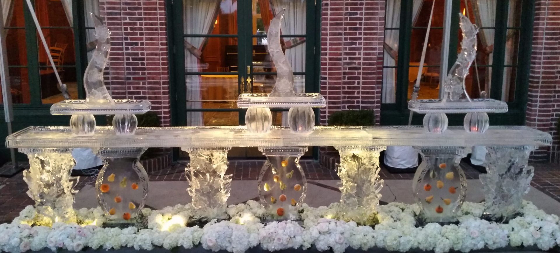 Decorative white floral arrangement and urns on a stone fountain in front of a brick building