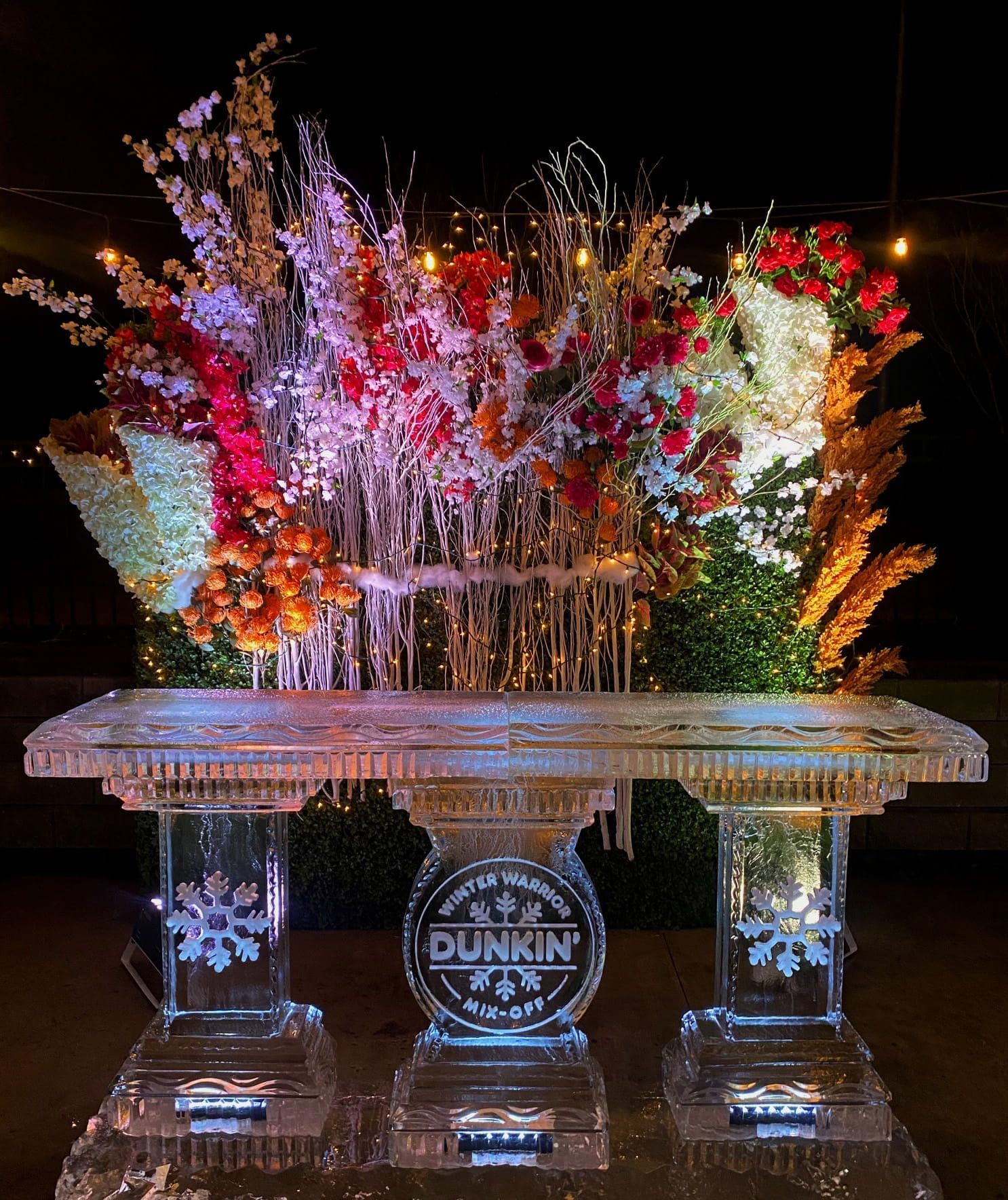 Lit floral ice sculpture with colorful flowers and Dunkin’ logo at the base
