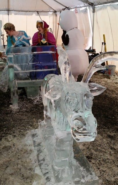 Ice sculpture of a goat under a tent, with two people standing behind it.