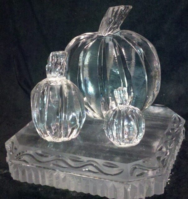 Clear glass pumpkin figurines on a decorative clear glass base against a dark background