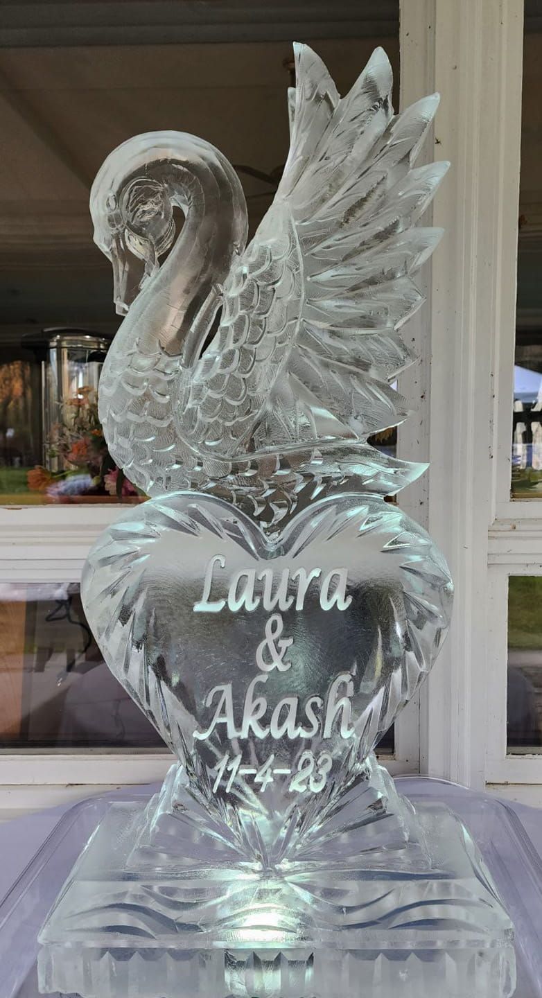 Clear ice sculpture of a swan with “Laura & Akash” etched on it, displayed on a pedestal.