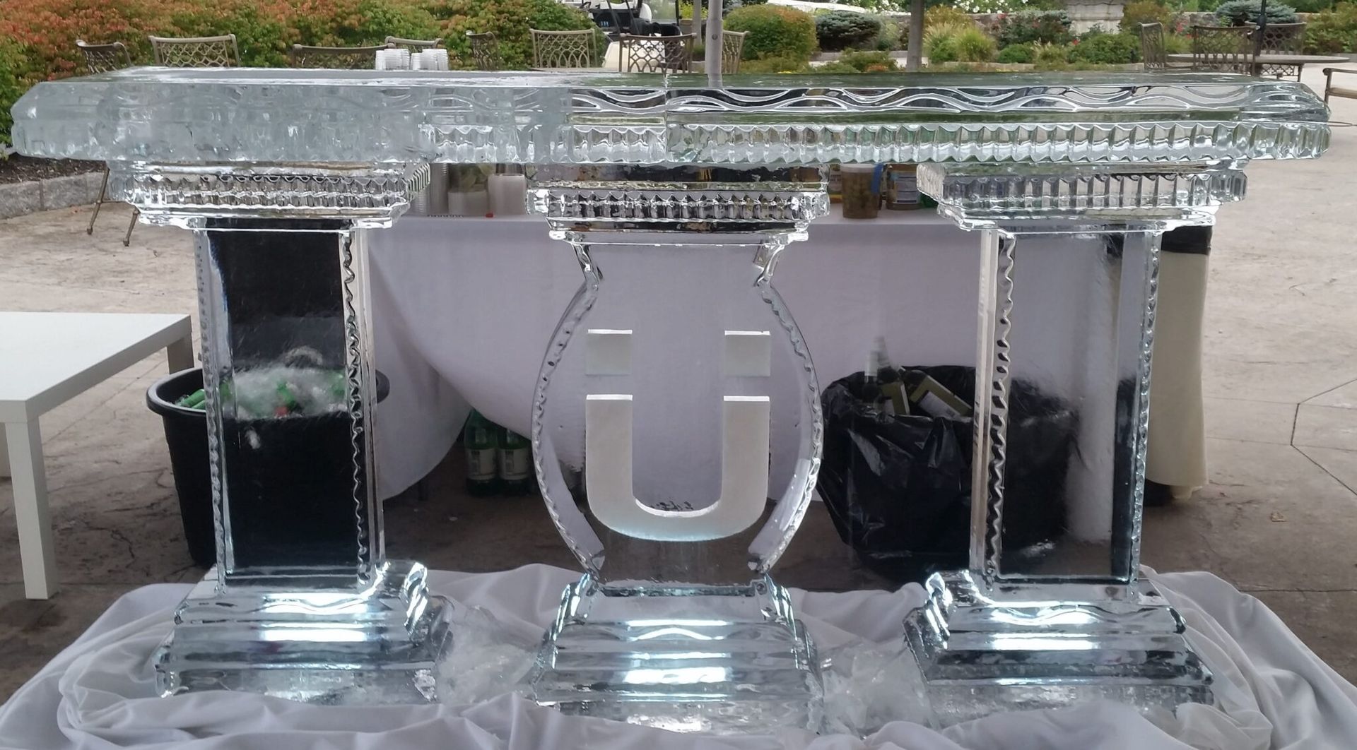 Clear glass trophy-like letters on a table, with a large U-shaped piece in the center outdoors