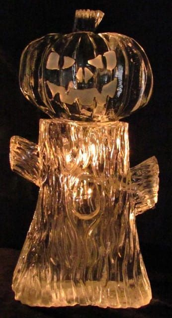 Glowing amber glass figurine shaped like a pumpkin-headed ghost on a black background