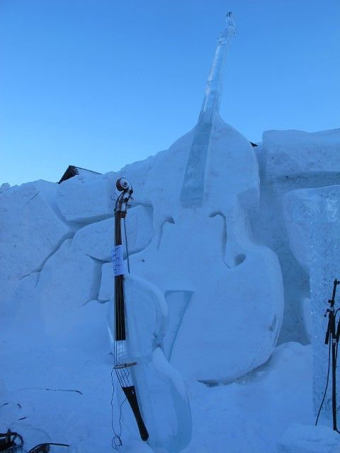 Snow-covered skis and poles leaning against a snowy wall under a clear blue sky.