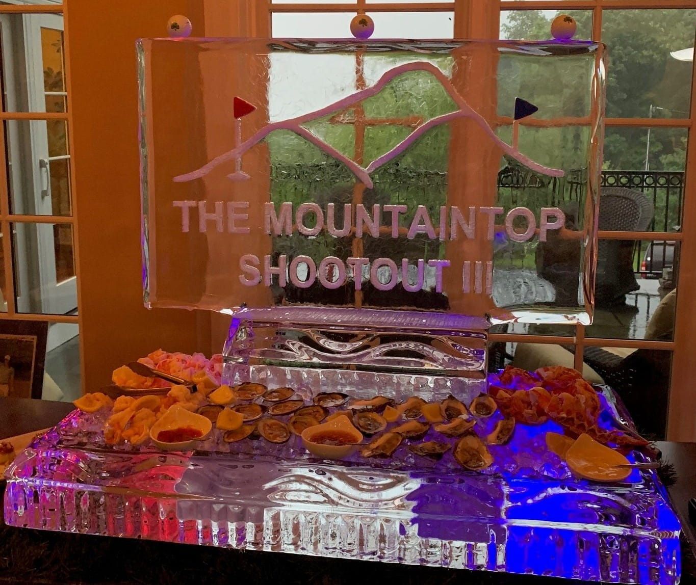 Clear acrylic trophy reading “THE MOUNTAIN TOP SHOOTOUT” on a silver tray with small orange treats