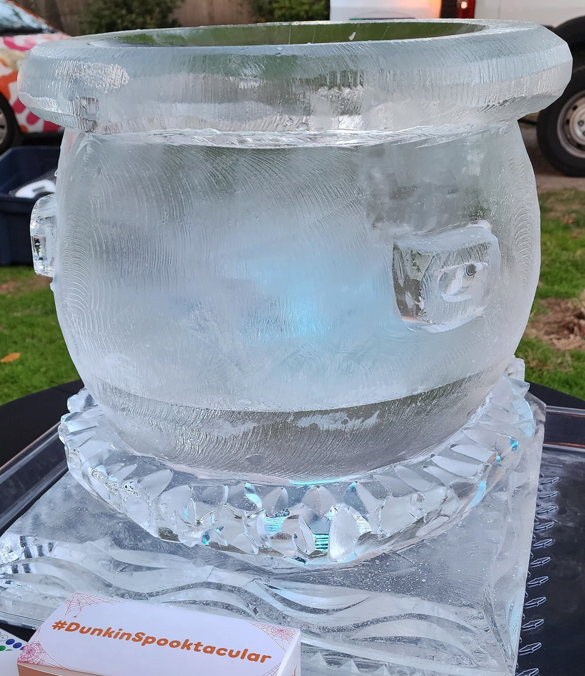 Clear ice sculpture on a decorative base outdoors, with a blue tint inside and frost on top