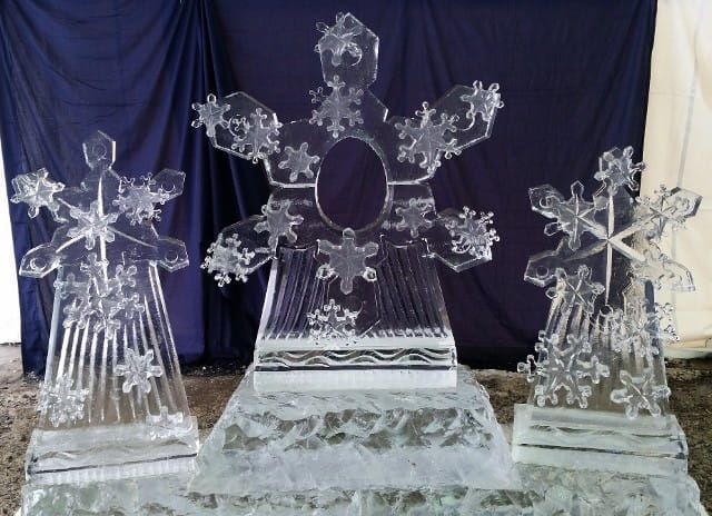 Three clear acrylic snowflake sculptures on tiered white stands against a dark blue backdrop.