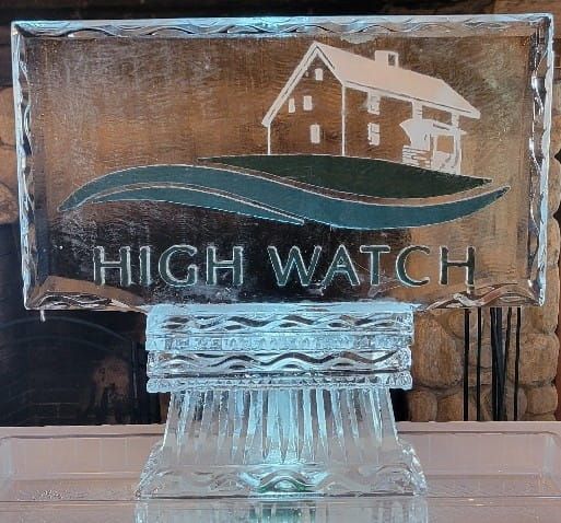 High Watch sign on a glass base, with a house logo and wavy blue and green background.