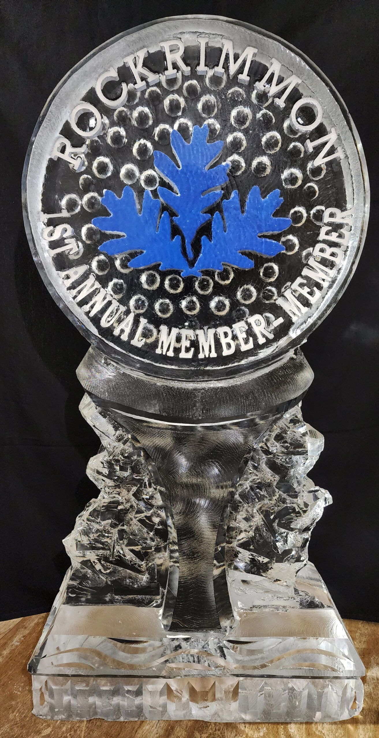 Clear glass trophy with a blue maple leaf and circular white lettering on a black background