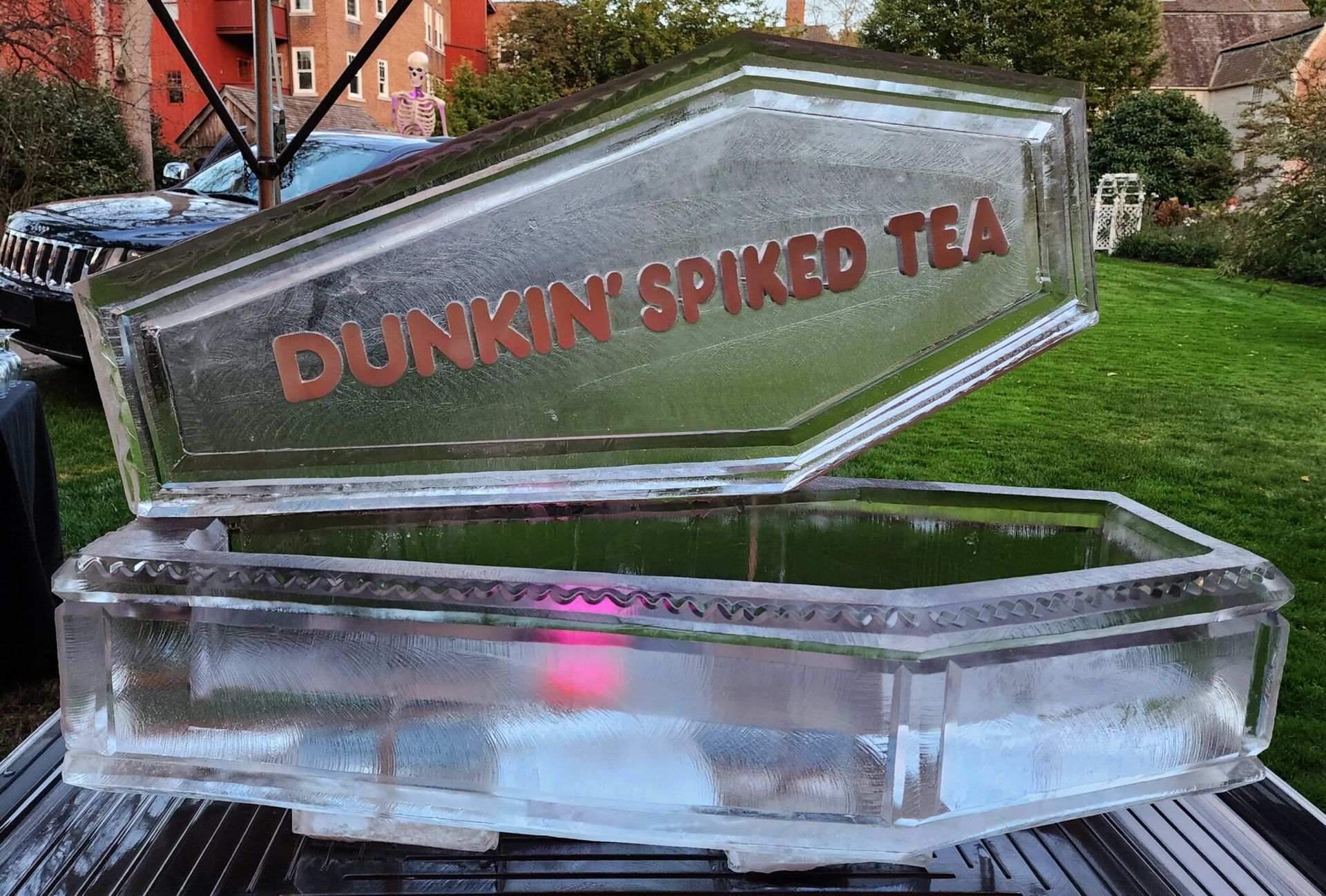 Clear ice sculpture of a tipped bottle labeled “Dunkin’ Spiked Tea” on a table outdoors