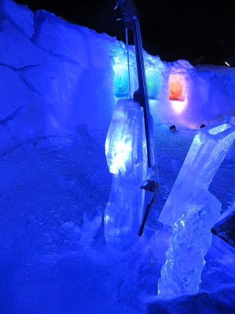 Blue-lit ice tunnel with carved ice walls and a glowing orange opening in the distance